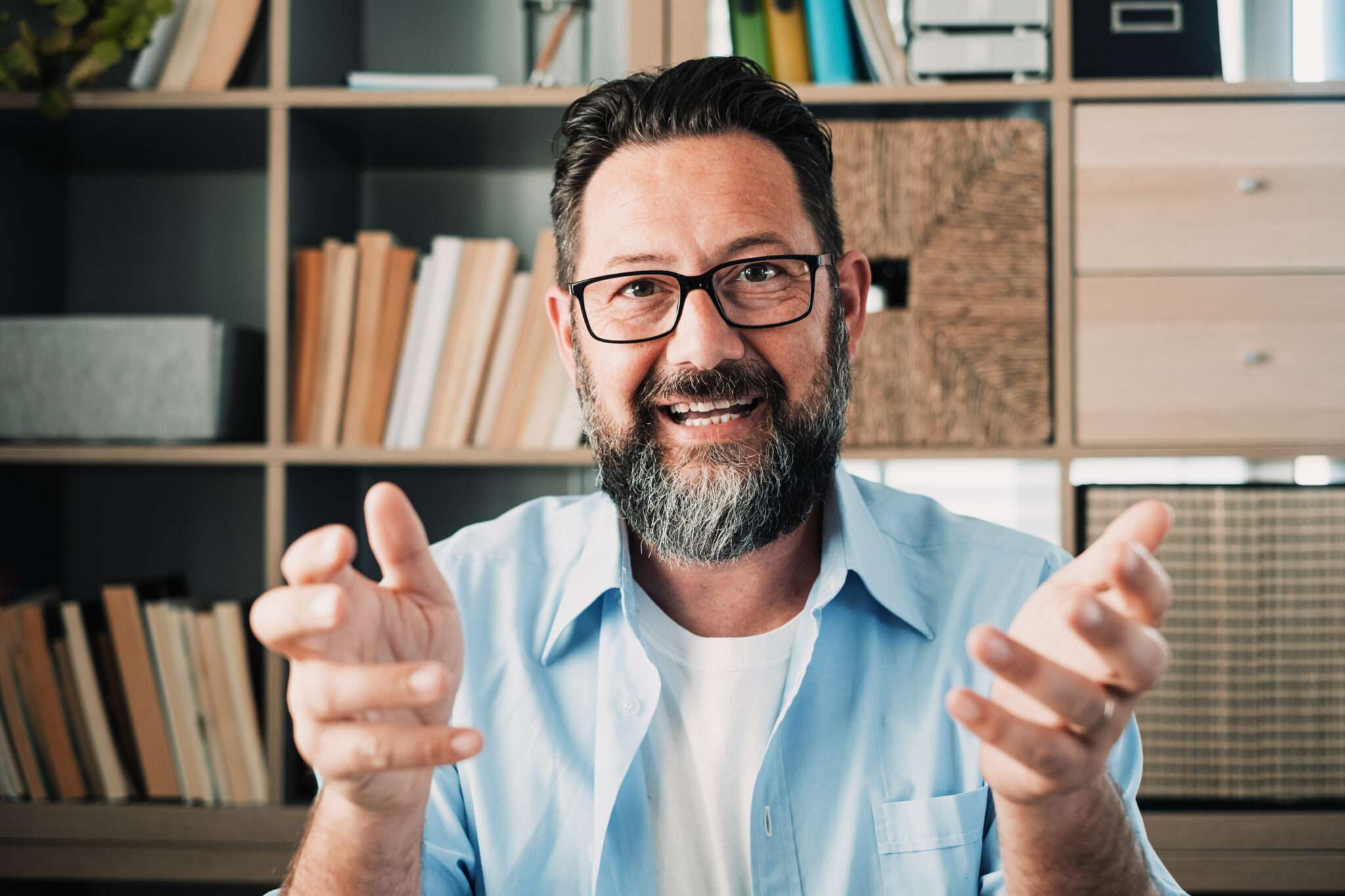 眼鏡をかけたひげを生やした男性が、フランスに関する本でいっぱいの本棚の前で身振り手振りをしている。