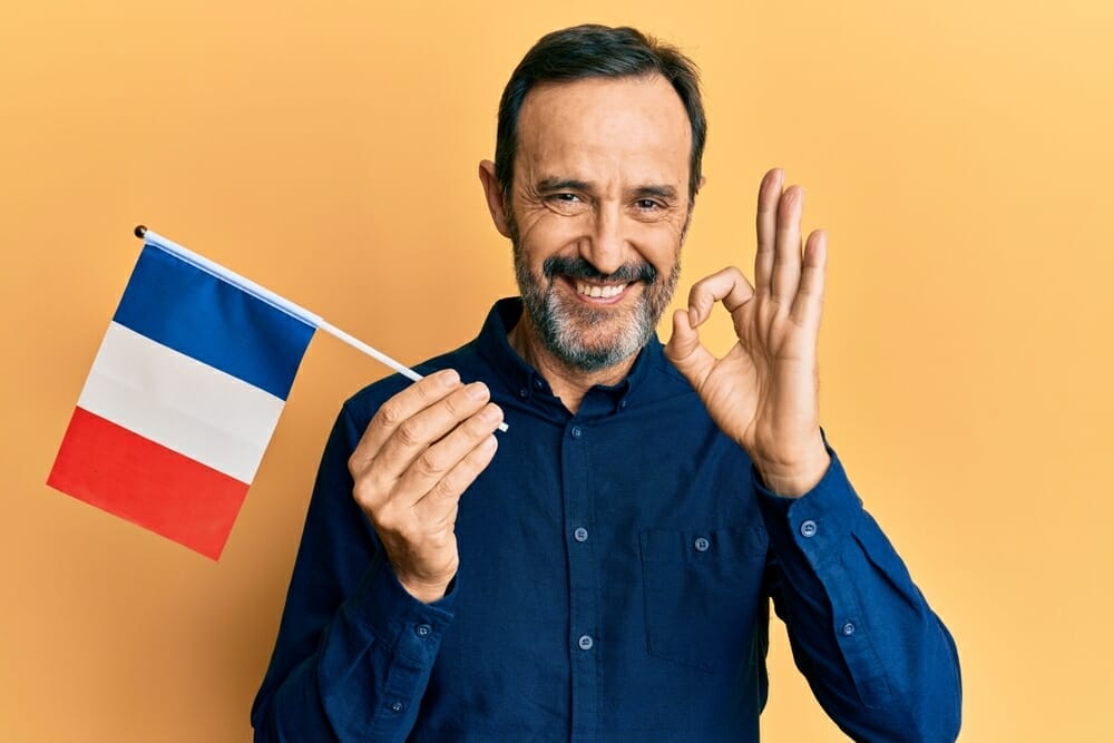 フランスの国旗を持ちながらOKのジェスチャーをする男性。