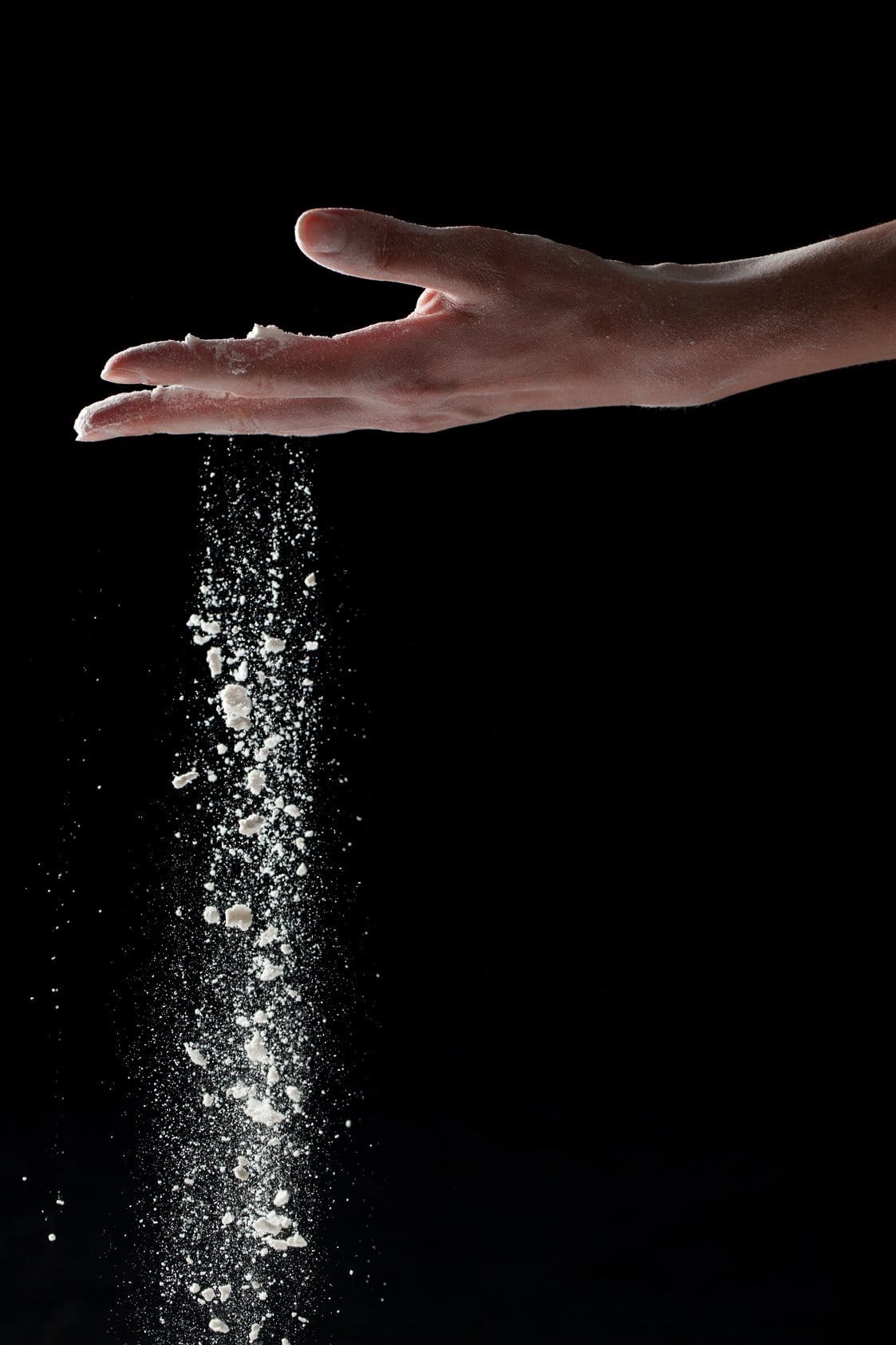 フランスで、黒い背景に振りかけられた塩に手を伸ばしている人。