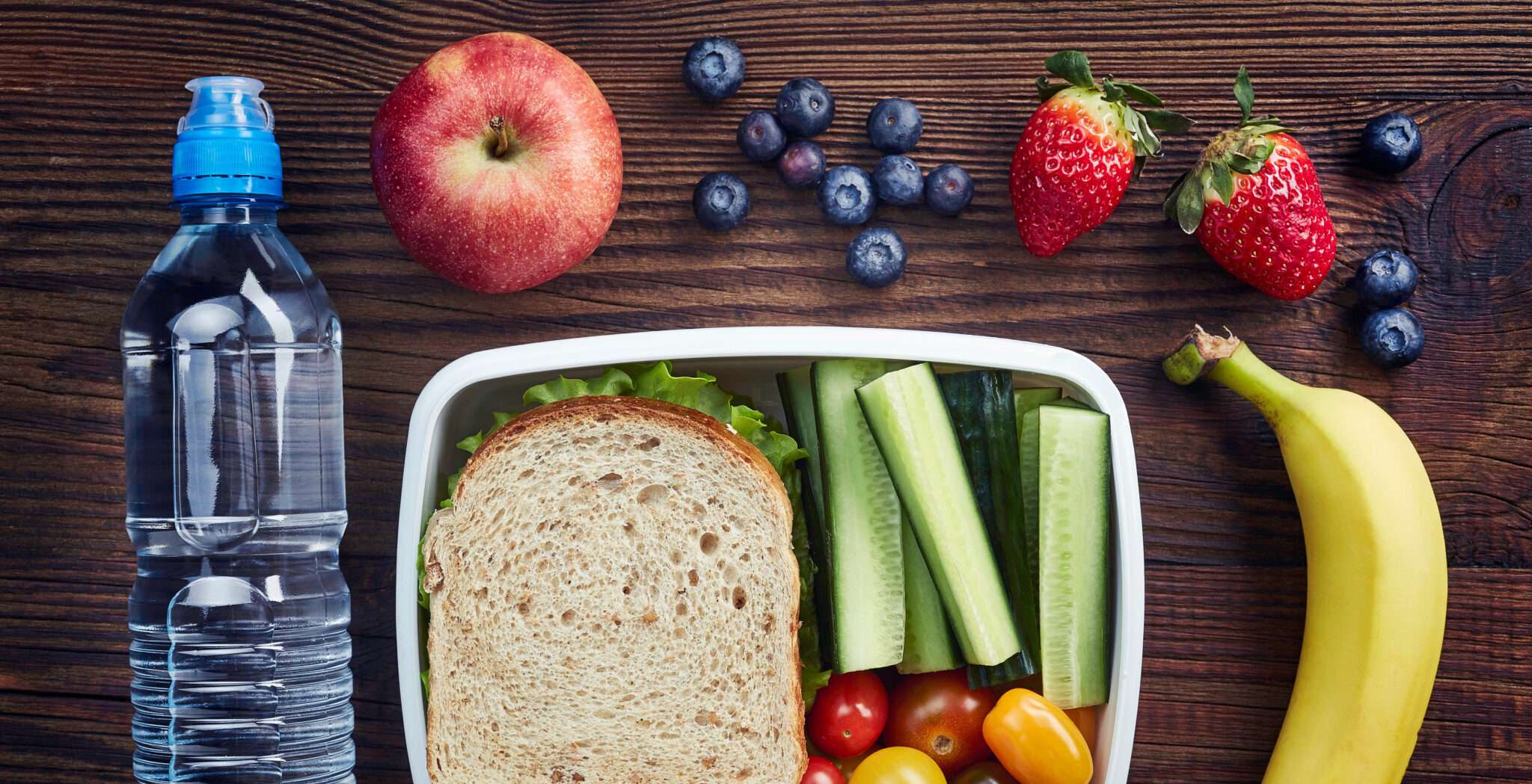 フランスの木のテーブルの上にサンドイッチ、フルーツ、水が入ったランチボックス。