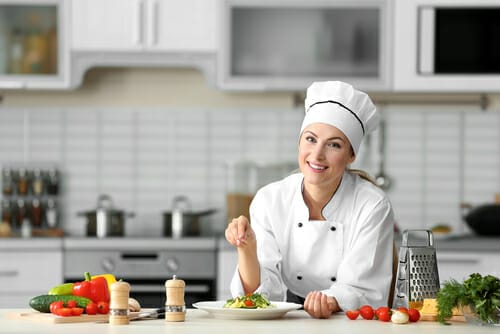 シェフの帽子をかぶった女性がキッチンでフランス料理を準備しています。 シェフの帽子をかぶった女性がキッチンでフランス料理を準備しています。