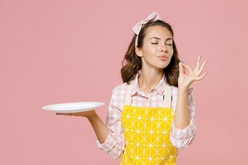 フランスで、エプロンを着て皿を持ち、OK のジェスチャーをする若い女性。