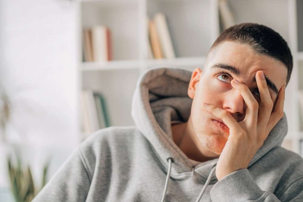 フランス滞在中、顔に手を当てているグレーのパーカーを着た男性。 フランス滞在中、顔に手を当てているグレーのパーカーを着た男性。