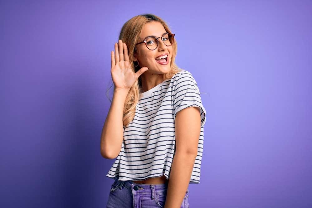 メガネをかけ、フランスから来た縞模様のシャツを着て耳を手で覆った若い女性。