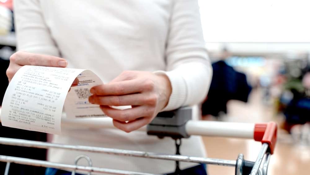 白い長袖シャツを着た人が店内の通路でショッピングカートの上に買い物レシートを持っており、フランスの日常的な市場の光景を彷彿とさせます。 白い長袖シャツを着た人が店内の通路でショッピングカートの上に買い物レシートを持っており、フランスの日常的な市場の光景を彷彿とさせます。