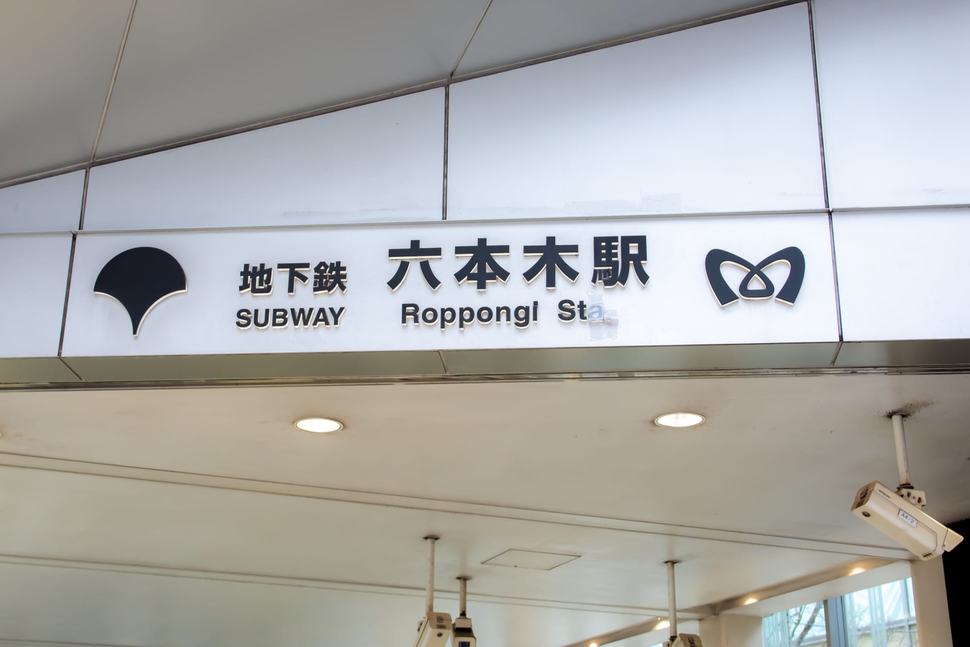 東京の六本木駅の標識。地下鉄のシンボルと日本語、英語、フランス語のテキストが特徴です。.
