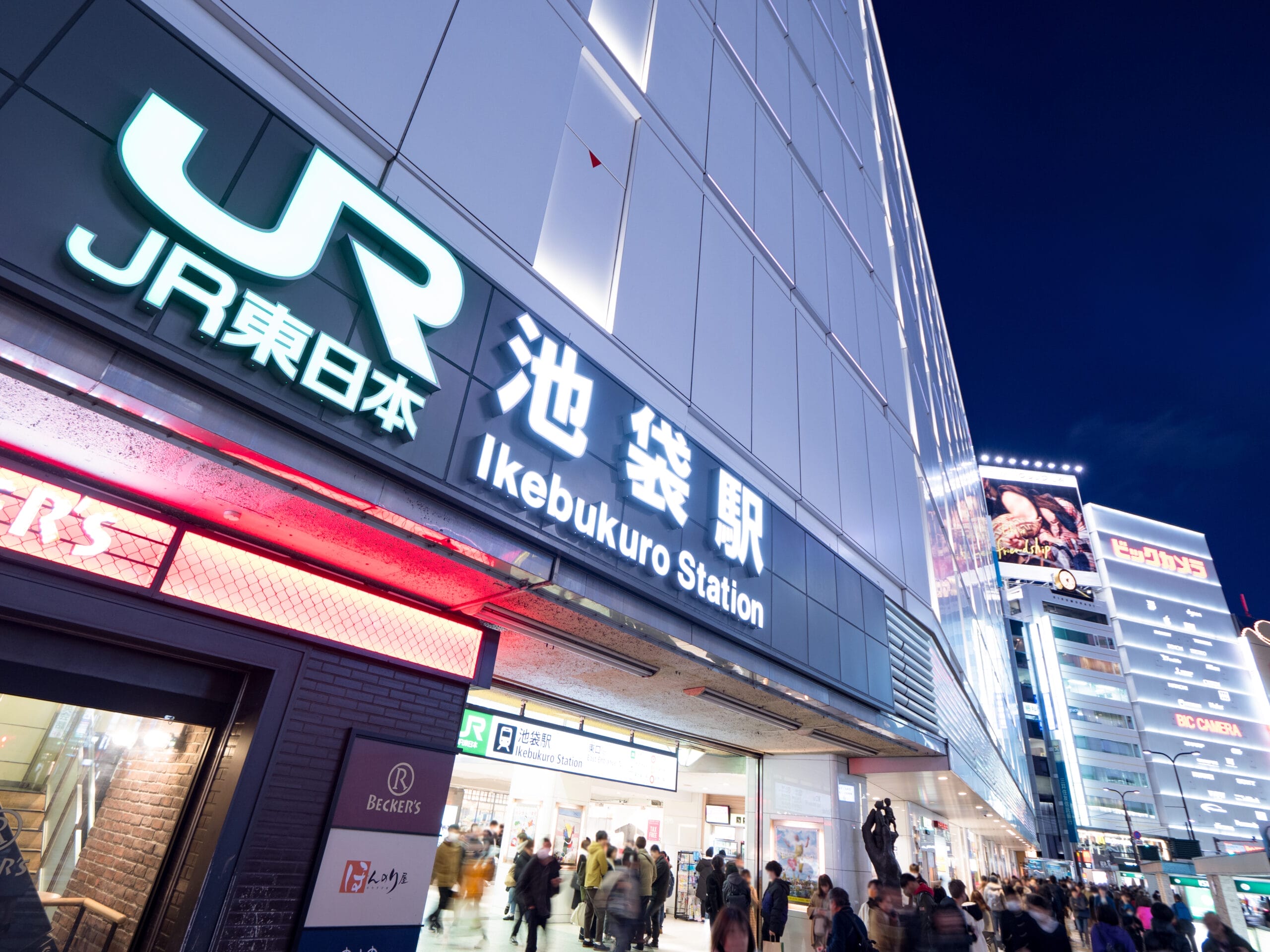 東京の池袋駅入口のストリートビュー。照明付きの看板と出入りする人々が、フランス語教室マンツーマンの授業近くのにぎやかな風景を思い出させます。.