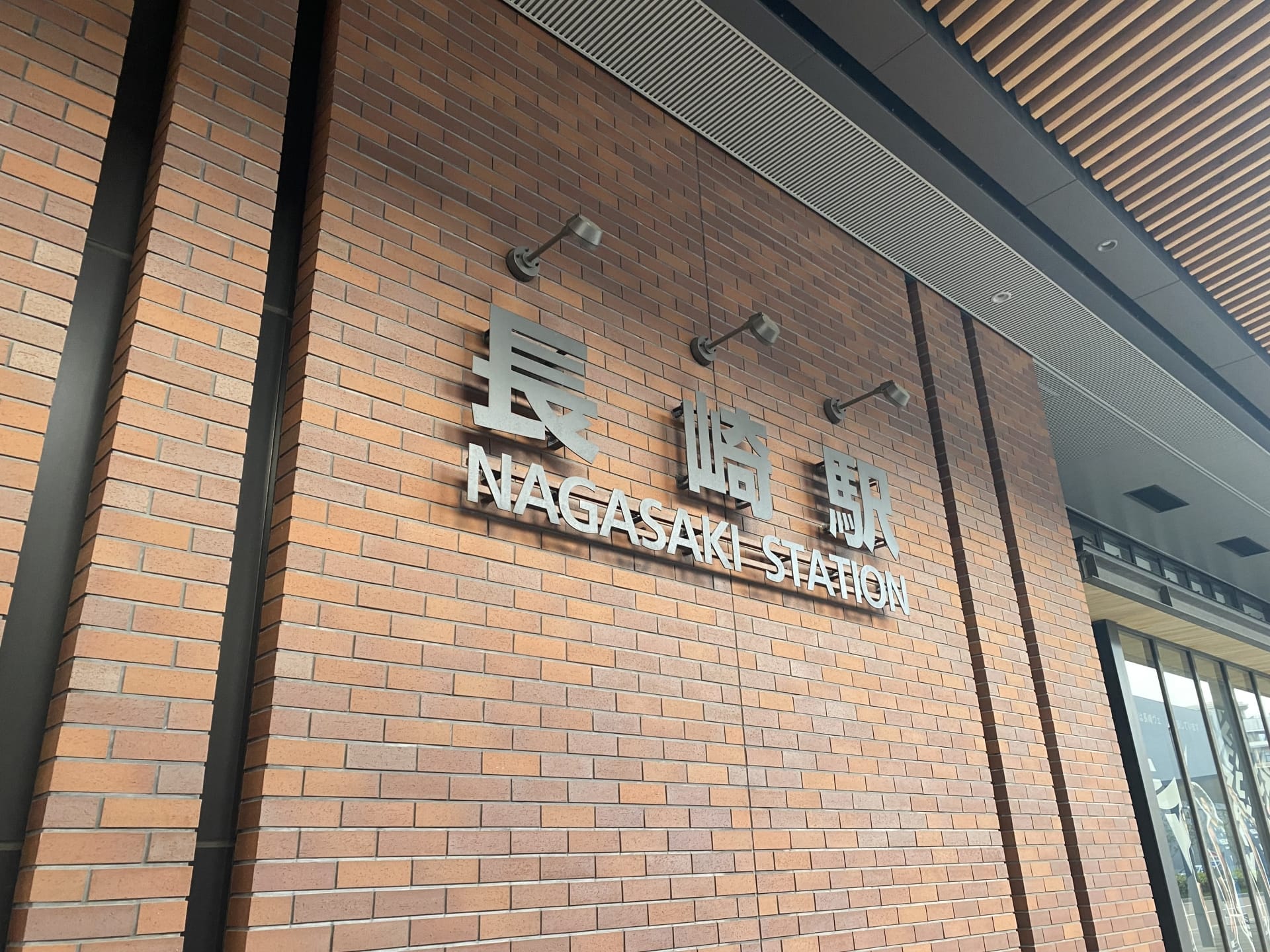 レンガの壁には日本語と英語で「長崎駅」の標識が飾られ、スラット屋根の下に収まっています。.