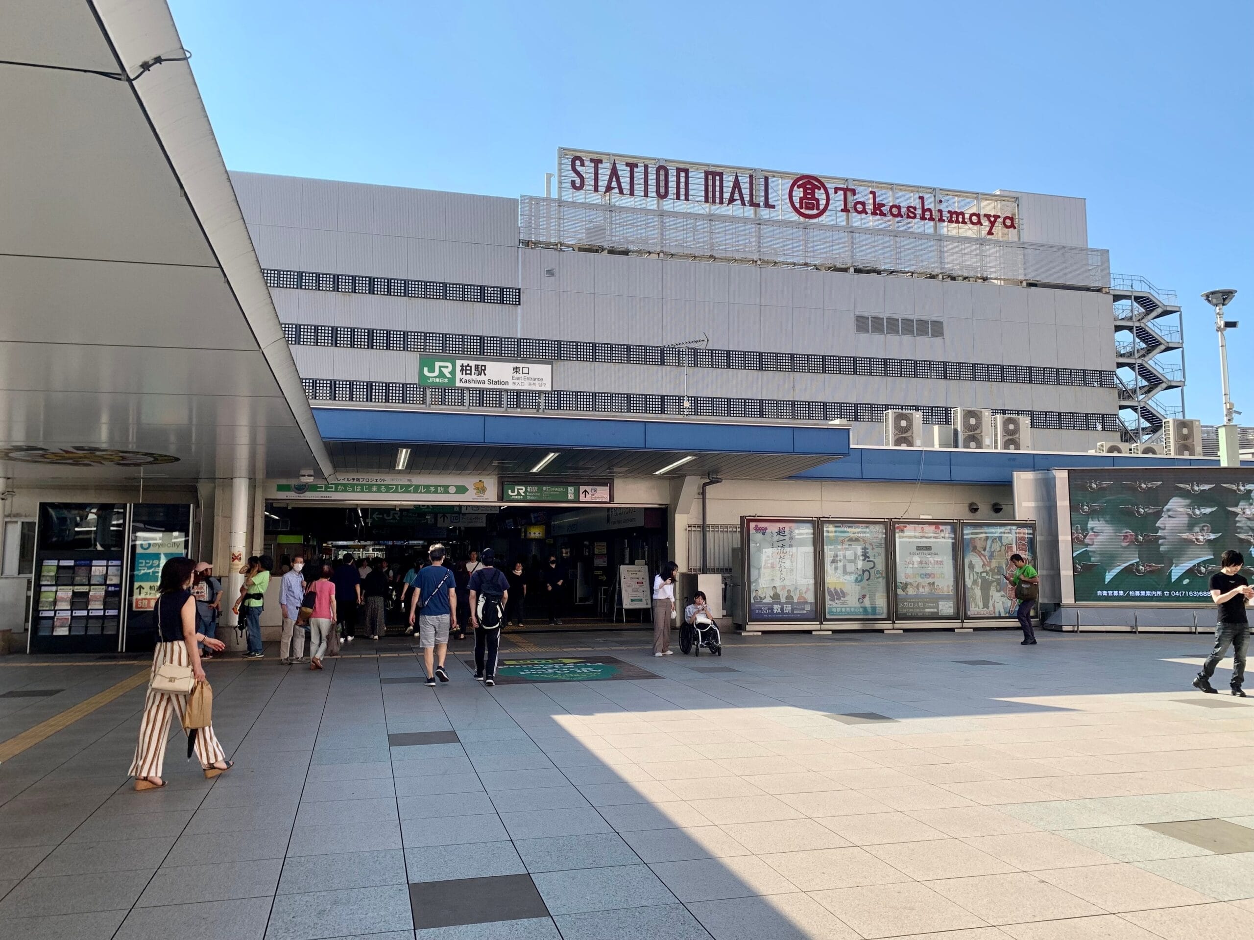 行き交う人で賑わう柏のステーションモールの入り口。高島屋の看板が頂上に飾られたこの建物は、晴れた空の下、タイル張りの前景を見せて立っています。近くのフランス語教室マンツーマンでは、個人に合わせた語学レッスンを提供しています。.