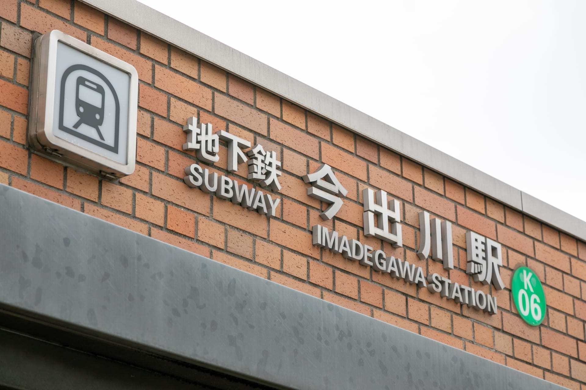 今出川駅のレンガ壁の標識には、地下鉄のアイコンと日本語、英語、フランス語の文字が描かれており、駅コード K06 が強調されています。活気に満ちた雰囲気は京都の多文化の本質を反映しており、マンツーマンのフランス語クラスに最適な場所です。.